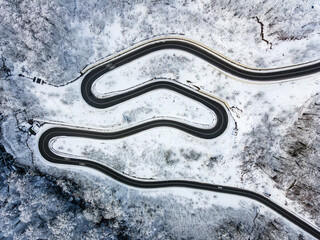 Top view of empty road along winter forest after snowfall. Aerial view of winding road through trees covered with snow
