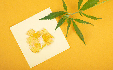 amber drops of cannabis wax with green marijuana leaf close-up, resin high in thc on a yellow...