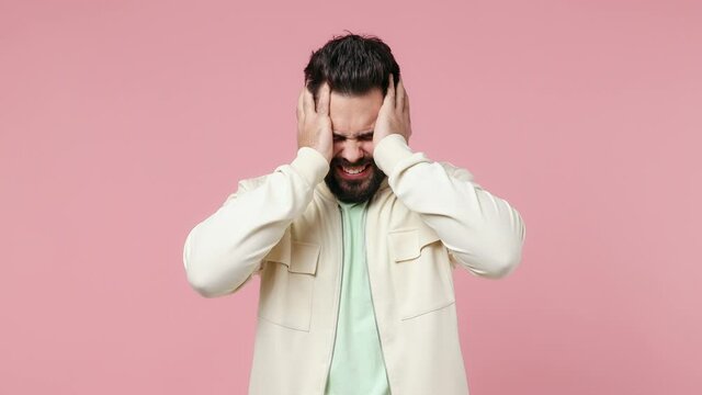 Displeased irritated angry young bearded brunet man 20s years old wears white shirt closed eyes cover ears do not want to listen scream isolated on plain pastel light pink background studio portrait