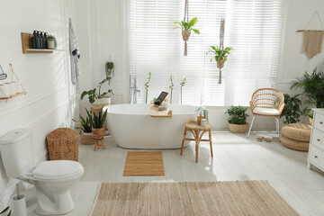 Stylish white tub and green houseplants in bathroom. Interior design