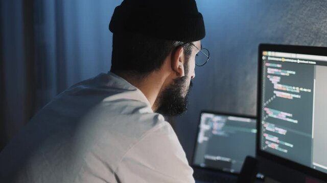 Young man mobile developer writes program code on a computer, programmer work in home office.