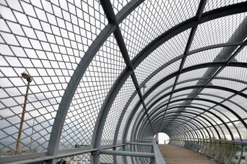 Metal tunnel bridge with wooden walkway.Strong metal bars bridge in shape of tunnel with wooden...