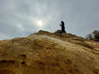 Silhouette of a man standing on top of a yellow rock under cloudy sky