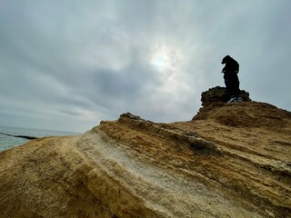 Unrecognizable man standing on top of a yellow rock at the seashore