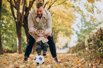 Naklejka na ściany i meble Father woth his little son in autumnal park playing with ball