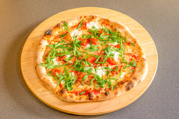 Pizza with burrata cheese, cherry tomatoes, arugula and serrano ham cooked in a stone oven