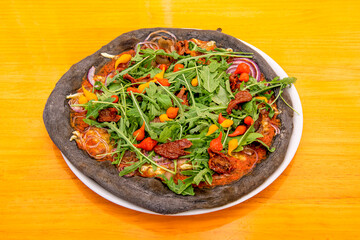 Charcoal flour pizza with arugula, red onion, dehydrated tomato, peppers and cheese