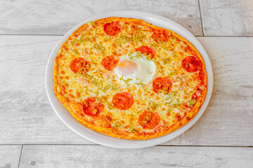 Pizza with spicy pepperoni, fried egg and vegetables with mozzarella cheese cooked in a stone oven