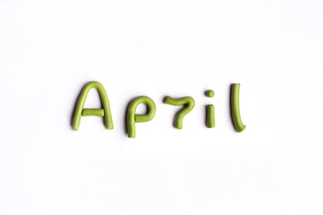The word April is made of light green plasticine on a white background