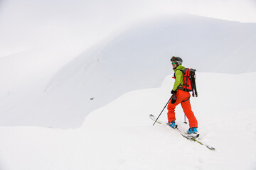 view of man skier with trekking poles walking along snowy mountain slope