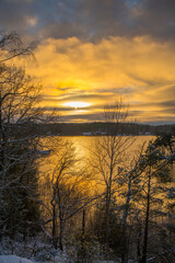 Fototapeta na wymiar Color full winter sun in solstice reflex in the calm lake Mälaren and trees in silhouette a winter day with snow in Stockholm