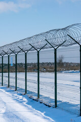 Iron fence with barbed wire in a snow-covered winter field against a blue sky. Fenced guarded territory, no access. Area protection and counteraction to illegal entry concept