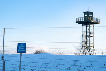 Surveillance tower, iron fence and caution banner with an inscription in Belarusian "Attention! State border of Ukraine. No entry". Closed area. Border protection and illegal migration concept