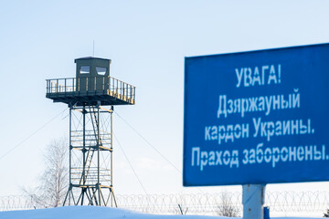 Blue caution plate with an inscription in Belarusian "Attention! State border of Ukraine. No entry" against the surveillance tower. Closed area. Counteraction to illegal migration concept