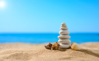 Fototapeta na wymiar Pebble tower with small seashells on the sunny beach against the backdrop of the sea. Summer theme. Selective focus on the tower.