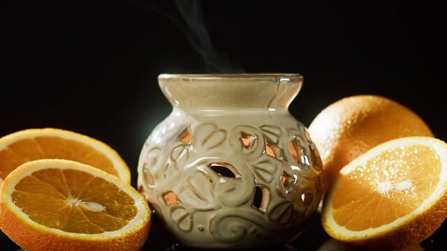 Candle holder and oranges close-up. Making aroma candles, oil diffuser on black background. Perfume for home, relaxing and spa concept. 