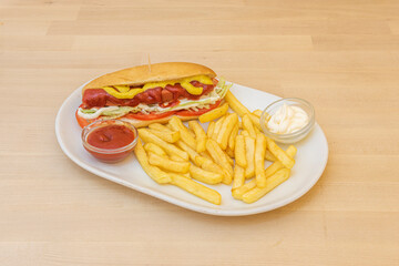 Hot dog with sausage, cheese with tomato slices, mustard, ketchup and mayonnaise on a white plate garnished with French fries