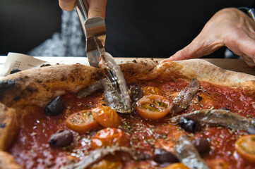 slicing pizza with artisan anchovies with tomato and mozzarella cheese