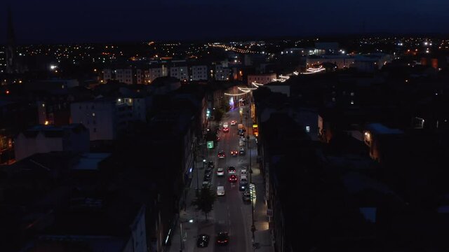 Fly above night city. Cars driving in streets of urban neighbourhood. Light decoration. Limerick, Ireland
