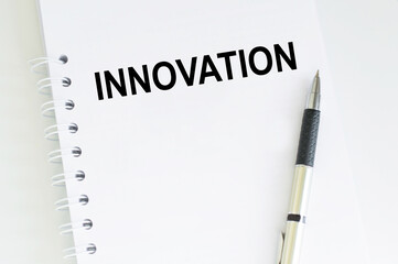 text INNOVATION on a white notepad with a pen on the table. Business concept