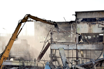 a modern powerful excavator cleans the rubble of a ruined building