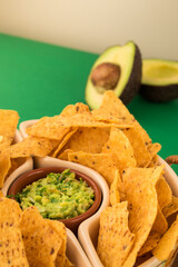 Some fried nachos in a pot with some fresh guacamole on a green surface 