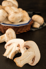 Cut champignon and some mushrooms in a basket on a black wooden table 