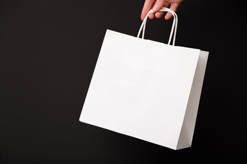 Female hand holding white blank shopping bag isolated on black background. Black friday sale,...