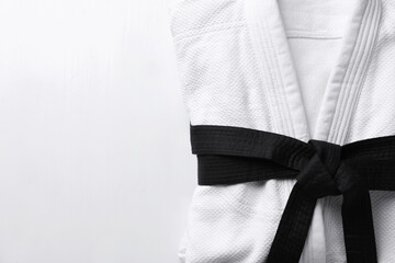 Martial arts uniform with black belt on white wooden background, top view. Space for text - obrazy, fototapety, plakaty
