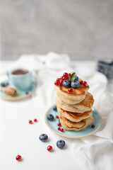 Homemade delicious pancakes with fresh blueberries, raspberries and honey syrup on white table against light background