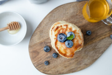 Blueberry pancakes served with honey on wood on a light background, copy space. Summer homemade breakfast.