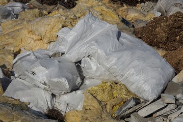 garbage from white bags and pieces of yellow glass wool in a heap in nature on a sunny day