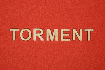 Fototapeta na wymiar text the word torment from gray wooden small letters on an red table