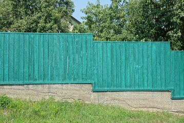 green private wooden fence wall on gray concrete foundation outdoors