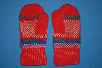 two red winter woolen mittens with a pattern lie on a blue table