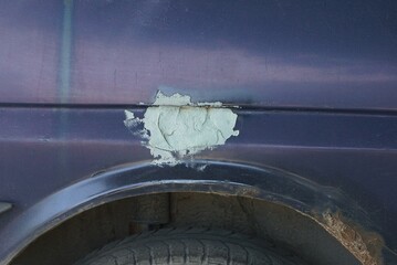 part of the car being repaired with a gray putty spot on the blue metal fenders