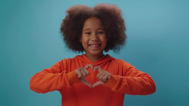 Smiling African American girl making heart shape with fingers looking at camera. Lovely kid holding hand heart symbol.