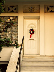 Fototapeta premium Christmas wreath decorated house entrance white door, with white marble stairs. Athens, Greece.