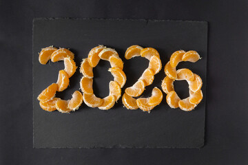 New Year 2026 is approaching. The figures are laid out with mandarin slices on a black background, top view.