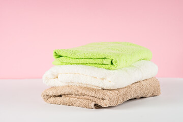 Obraz na płótnie Canvas Bath towel stack at bathroom. White, beige and green towels at pink background.