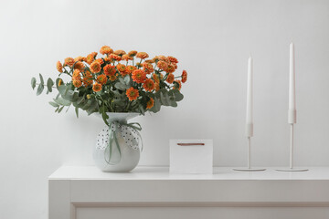 composition with flowers in a vase, candles and a blank card for text, a bouquet of orange...