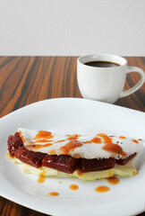Brazilian snack called 'Tapioca' stuffed with guava paste and white cheesse with a cup of coffee in the background. Brazilian food.