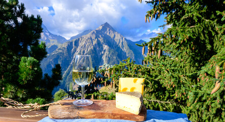 Glass of swiss or savoy dry white wine, tomme and  emmental cheese with Alpine mountains peaks on...