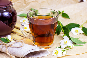 Fresh organic aromatic glass herbal tea cup with white jasmine flowers on light background.