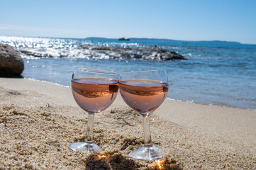 Two glasses of local rose wine on white sandy beach and blue Mediterranean sea on background, near Le Lavandou, Provence, France