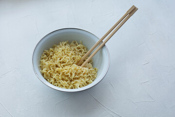 Instant noodles in a bowl with wooden chopsticks on a white textured background.