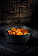 Yellow beans in a black bowl. Boiled beans with meat on a stone table. Beans with tomato sauce and pork. Contrasting dramatic light as an artistic effect.