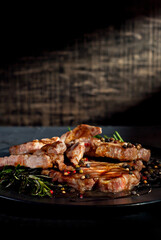Steak with sauce on a black plate. Meat with spices and rosemary on a dark background. Contrasting light as an artistic effect. Copy space and free space for text near food.