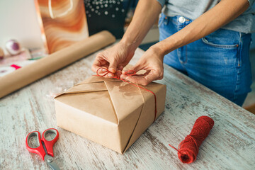 Young woman wrapping a gift, decorating stylish gift in craft paper on table in home