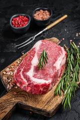 Fototapeta na wymiar Raw Rib-eye Steak, beef marbled meat on wooden board with rosemary. Black background. Top view